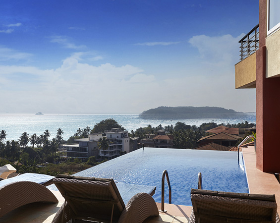 Goa sea-view villa featuring an infinity pool, lounge chairs, and a scenic coastline backdrop