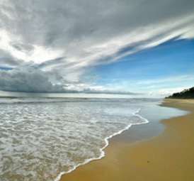Wide sandy beach with gentle waves under dramatic cloudy skies