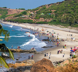 Scenic beach with rocky cliffs, blue waves, and tourist crowds