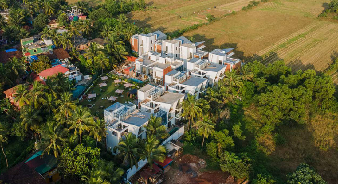 Aerial view of a white modern villa complex surrounded by coconut trees, farmland, and greenery in a rural area