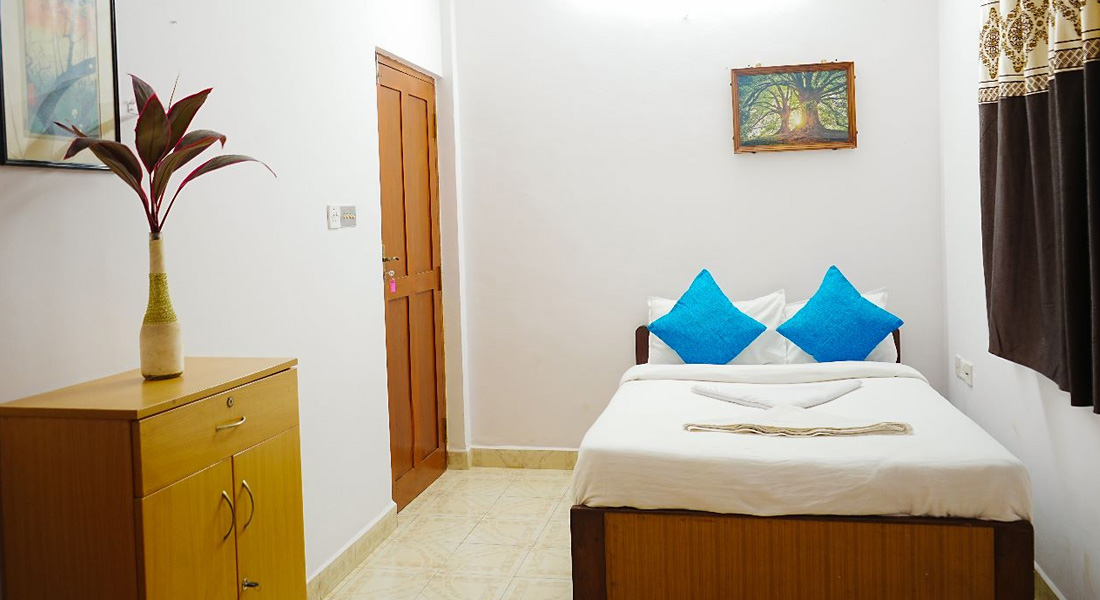 Simple private villa bedroom in Goa with double bed, blue pillows, wooden wardrobe, and curtains