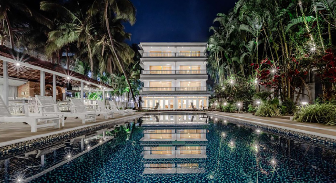 Luxury Goa villa with illuminated swimming pool, tropical palm trees, and modern multi-storey building at night