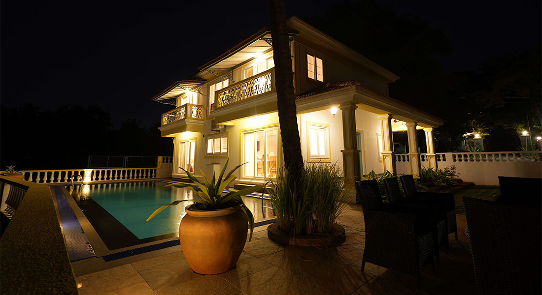 Two-storey villa at night with lights on, private swimming pool, balcony, and outdoor seating area