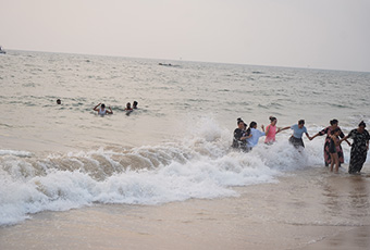 Visitors enjoying sea waves along the shoreline at Candolim Beach in Goa.