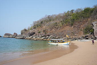 Secluded sandy cove at Butterfly Beach in Goa with a boat anchored near the shoreline and rocky hills in the background