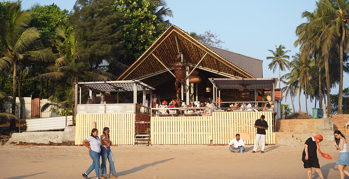 Beachside restaurant at Anjuna Beach in Goa with palm trees, visitors, and sandy shoreline during daytime