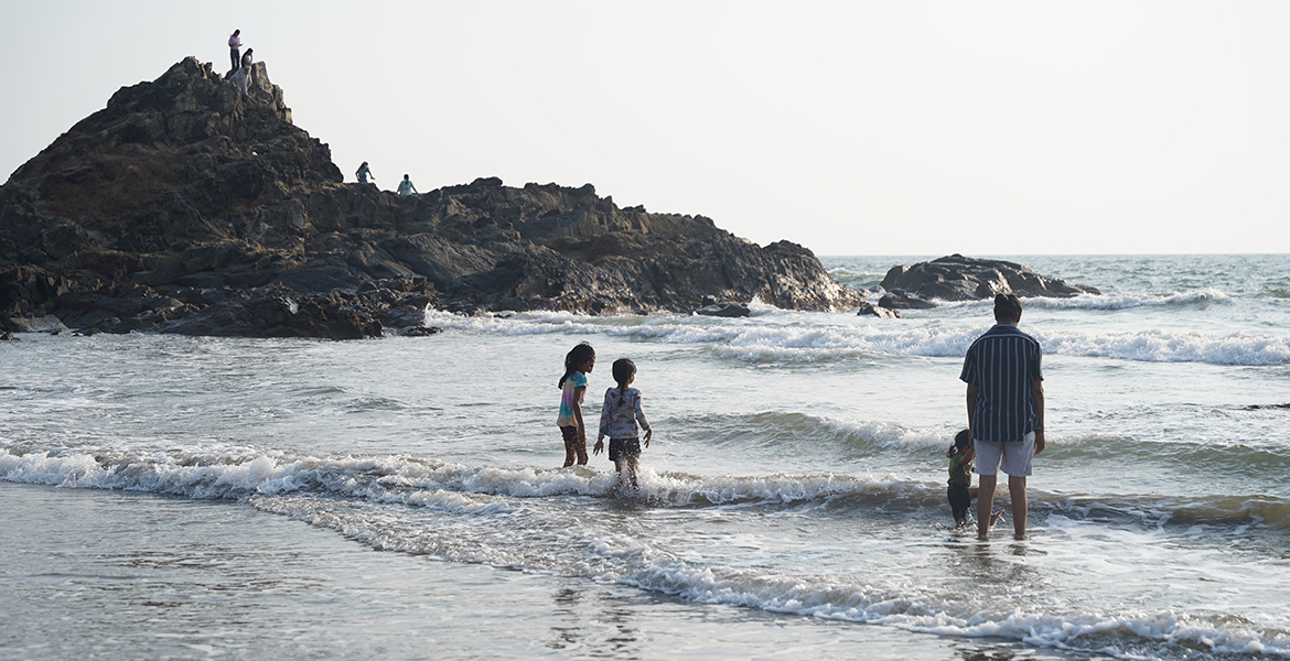 People enjoying sea waves near the rocky shoreline at Ozran Beach in Goa