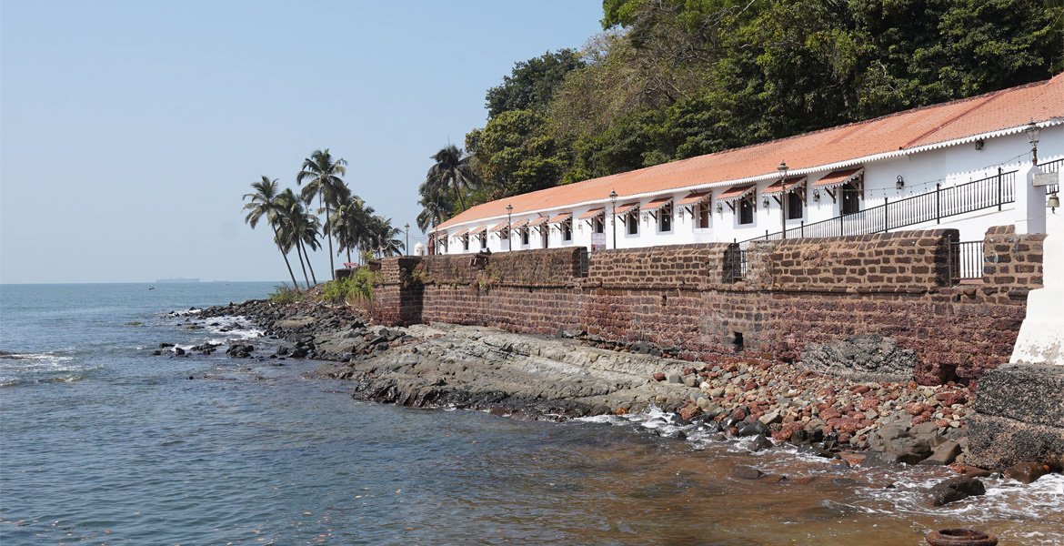 Aguada Jail Museum in Goa overlooking the Arabian Sea with historic stone walls, rocky shoreline and coconut palm trees