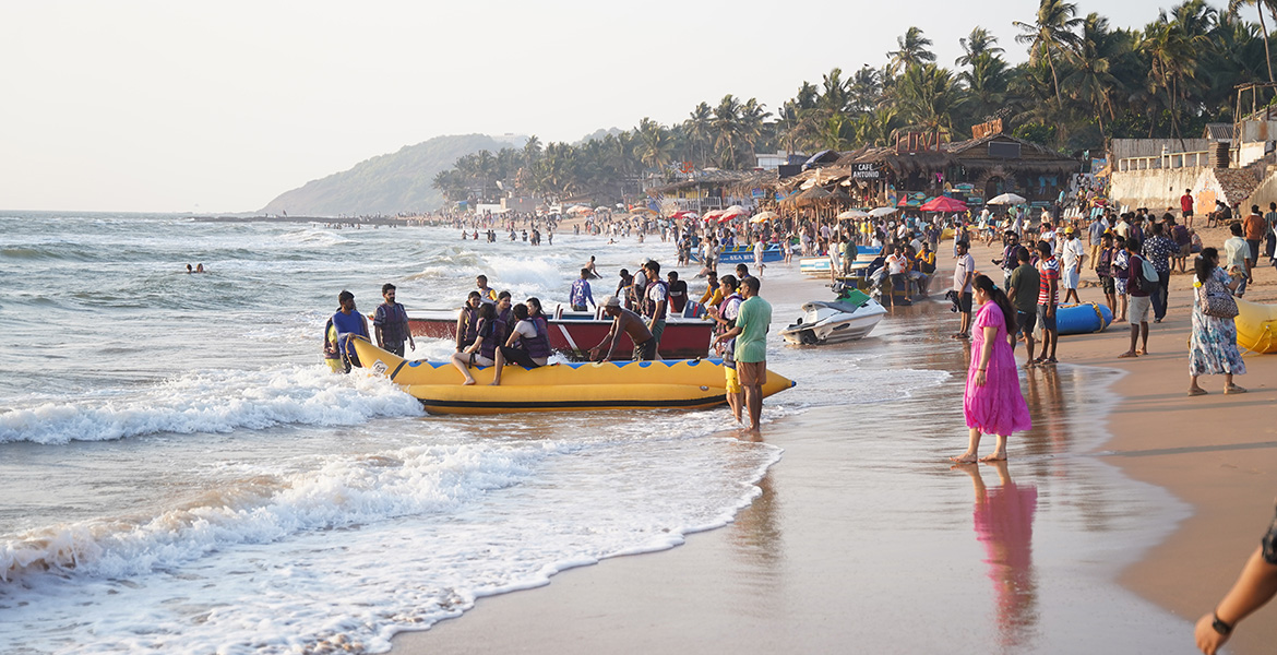 Tourists enjoying a banana boat ride at Anjuna Beach in Goa with crowded shoreline and beach shacks