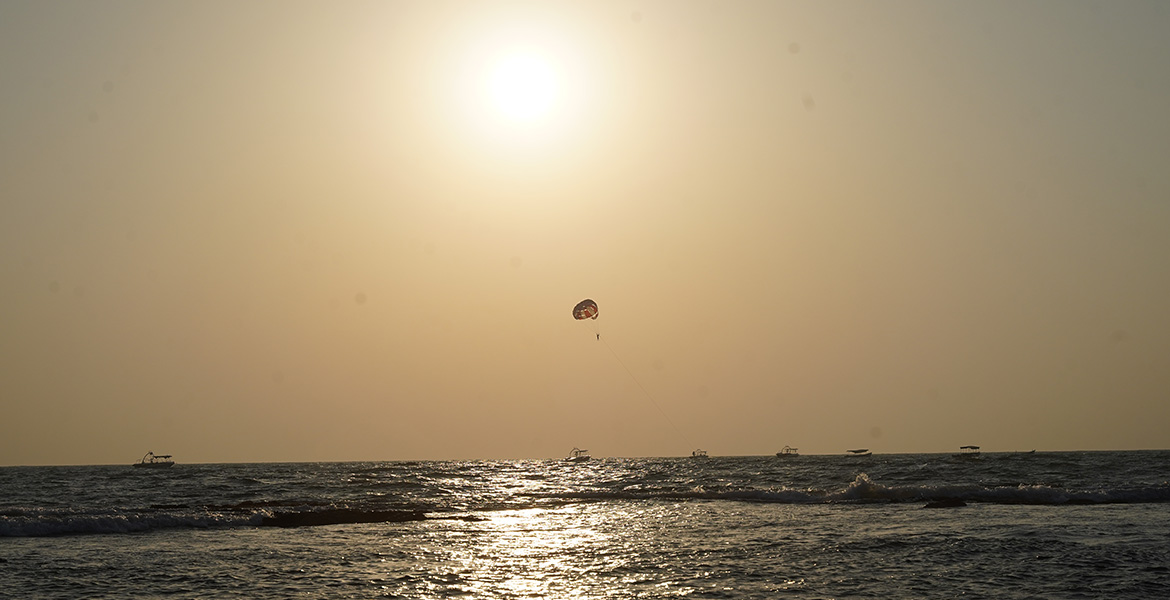 Parasailing activity at Anjuna Beach in Goa during sunset with sea waves and golden sky reflections