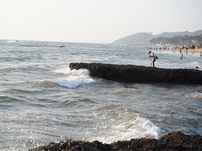 Rocky coastline with waves crashing against the shore at Anjuna Beach Goa, with visitors enjoying scenic sea views