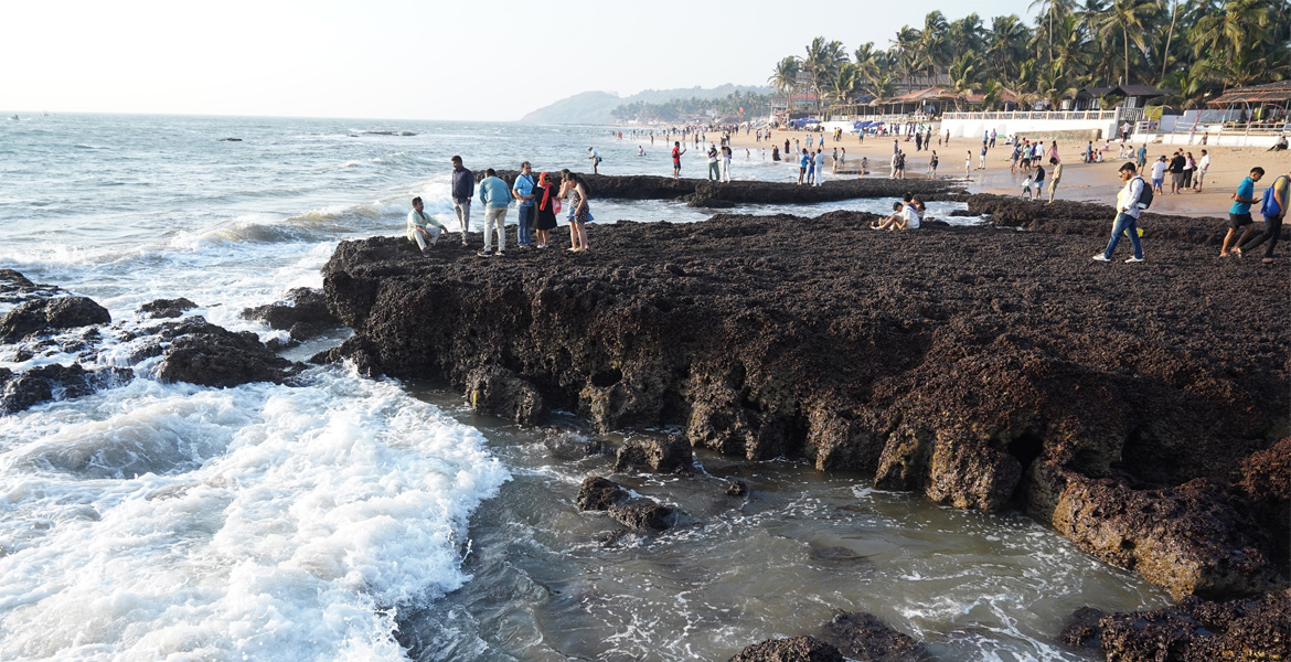 Anjuna Beach Goa rocky shoreline with waves and visitors