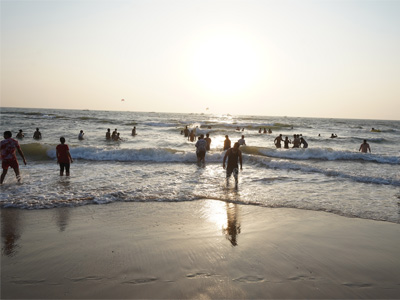 Visitors enjoying the waves and sunset at Anjuna Beach in North Goa along the Arabian Sea