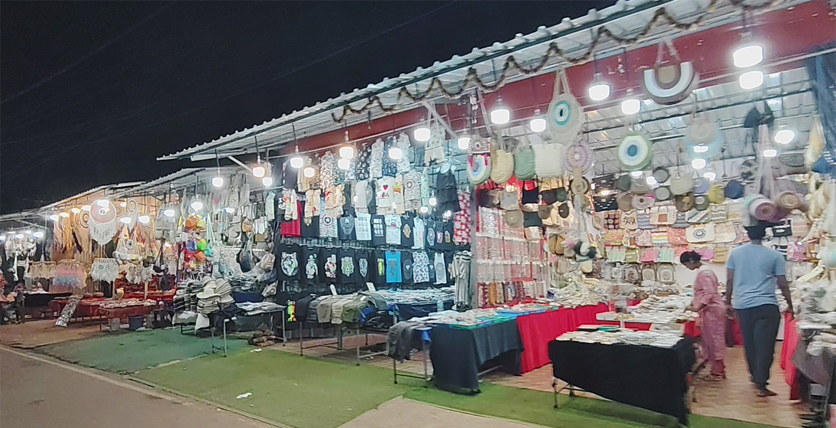 Shopping stalls displaying handicrafts, clothing, dreamcatchers, bags, and souvenirs at Anjuna Flea Market Goa