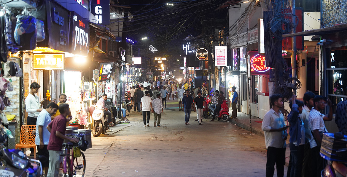 Busy nightlife street with shops, cafes and crowds in Baga, Goa at night.