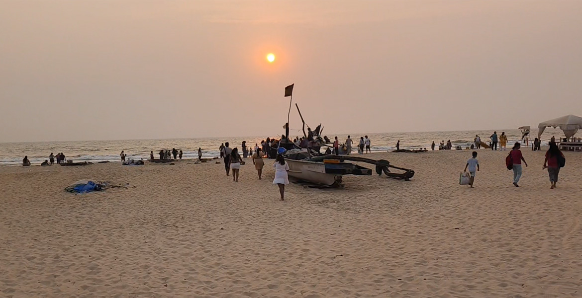 Tourists gathered around a traditional wooden fishing boat on Benaulim Beach during a golden sunset in South Goa