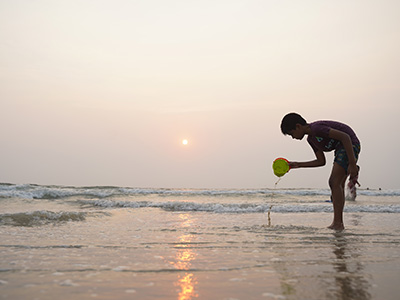 Child playing with a bucket at Benaulim Beach during sunset on the peaceful South Goa coastline
