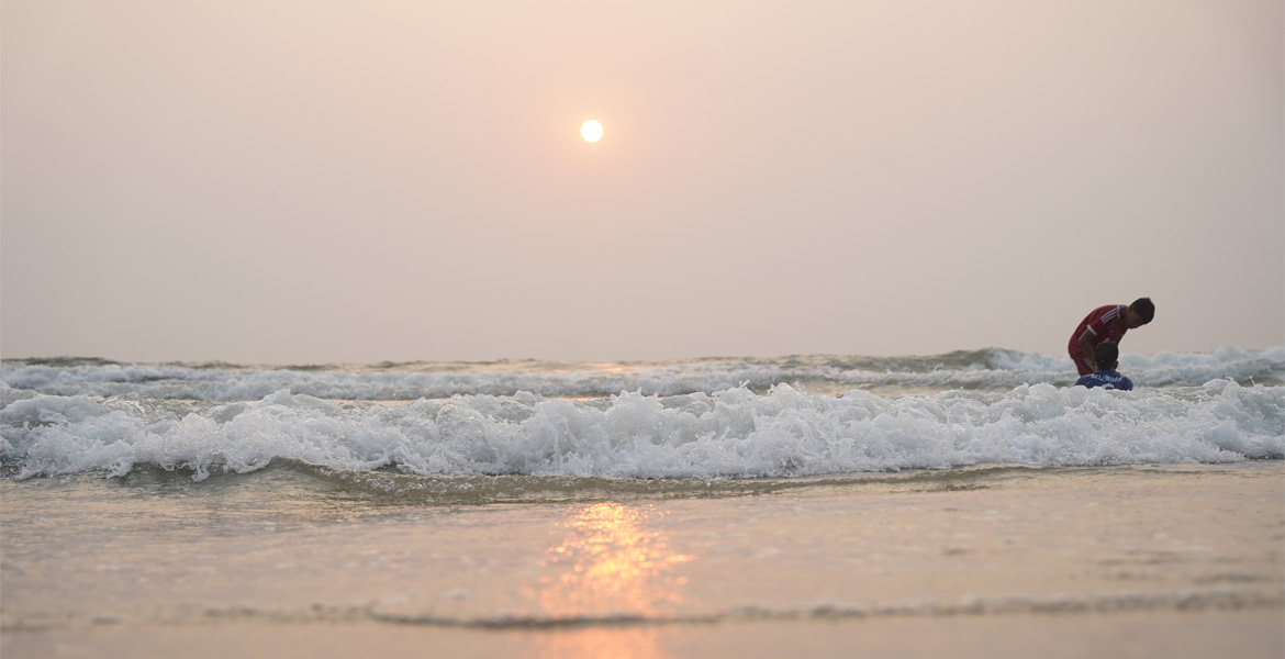 People enjoying the gentle waves at Benaulim Beach during a hazy sunset in South Goa