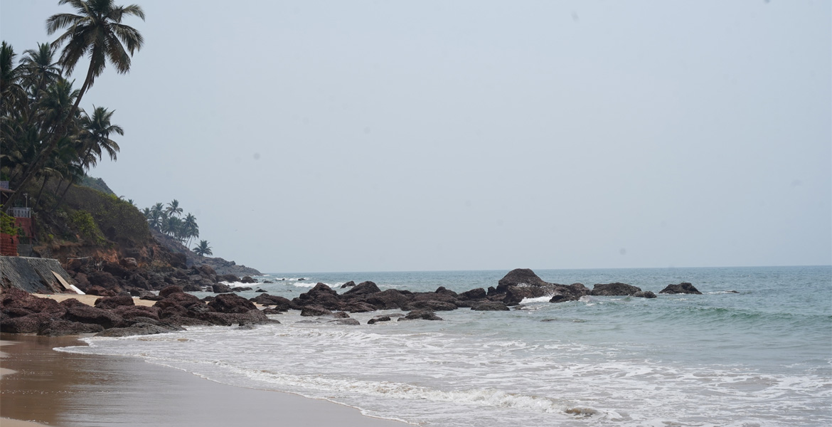 Rocky shoreline and gentle waves at Bogmalo Beach Goa, surrounded by palm trees and coastal scenery