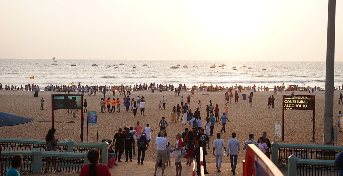 Evening crowd enjoying sunset view at Calangute Beach with boats in the Arabian Sea and beach entrance walkway in Goa