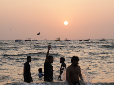 Visitors enjoying the sunset at Calangute Beach with boats and parasailing over the Arabian Sea in Goa