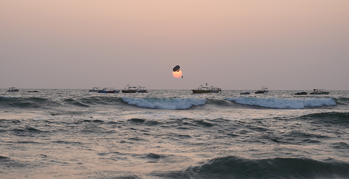 Sunset view at Calangute Beach with ocean waves, fishing boats, and parasailing activity over the Arabian Sea