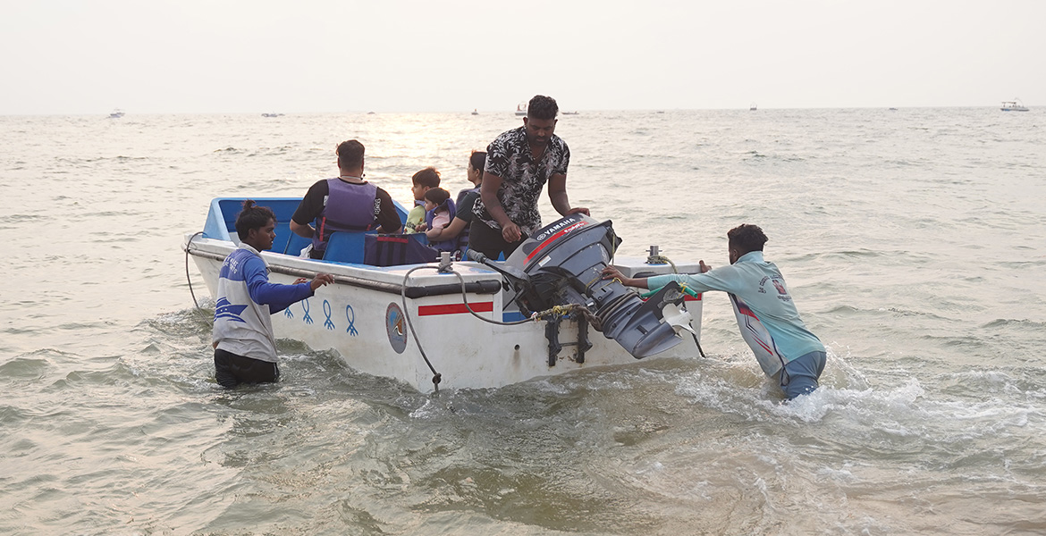 Tourists boarding a small motorboat for a sea ride at Candolim Beach in Goa during sunset