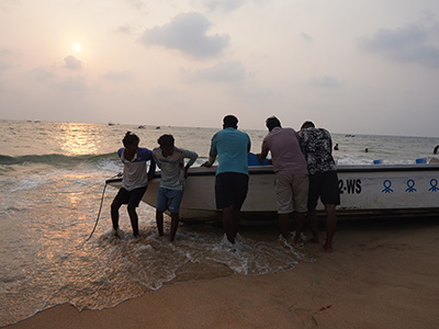 People pulling a fishing boat ashore during sunset at Candolim Beach in Goa