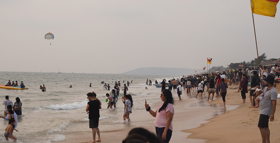 Tourists enjoying the sea, parasailing, and evening atmosphere at Candolim Beach in Goa
