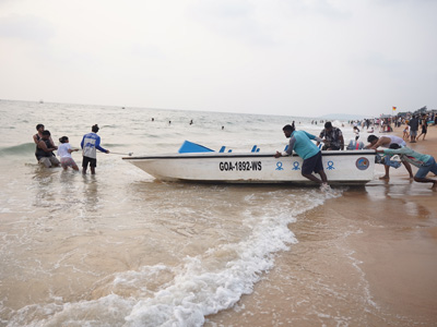 Visitors launching a speedboat from the shore at Candolim Beach in North Goa with people enjoying the beach