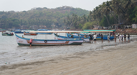 Tourist boats along the shoreline at Coco Beach in Goa with palm trees and coastal view