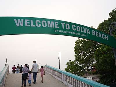 Visitors walking across the entrance bridge to Colva Beach Goa beneath the welcome arch