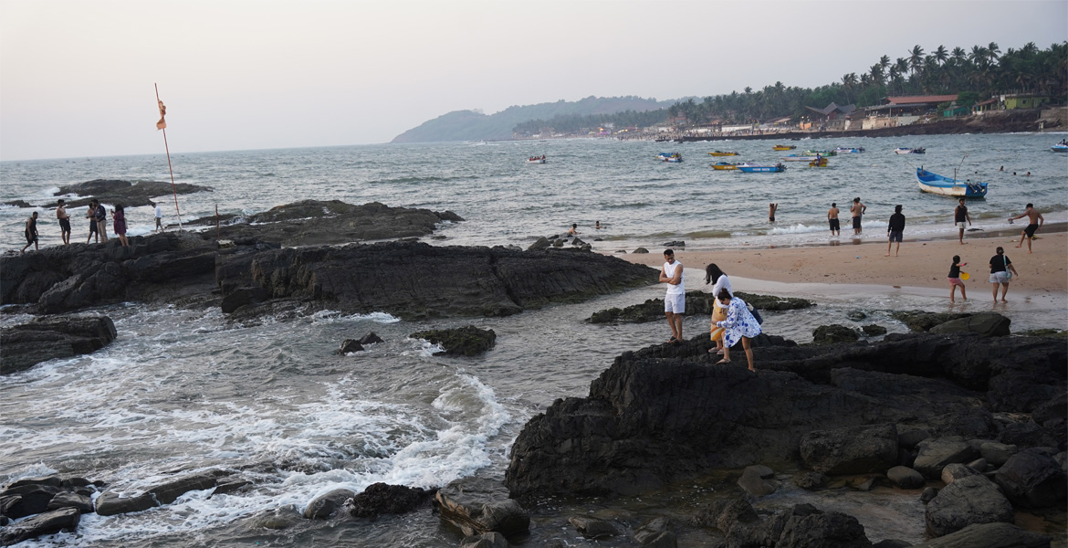 Panoramic view of the rocky shoreline and sandy beach at Curlies Beach Goa with visitors enjoying the coast