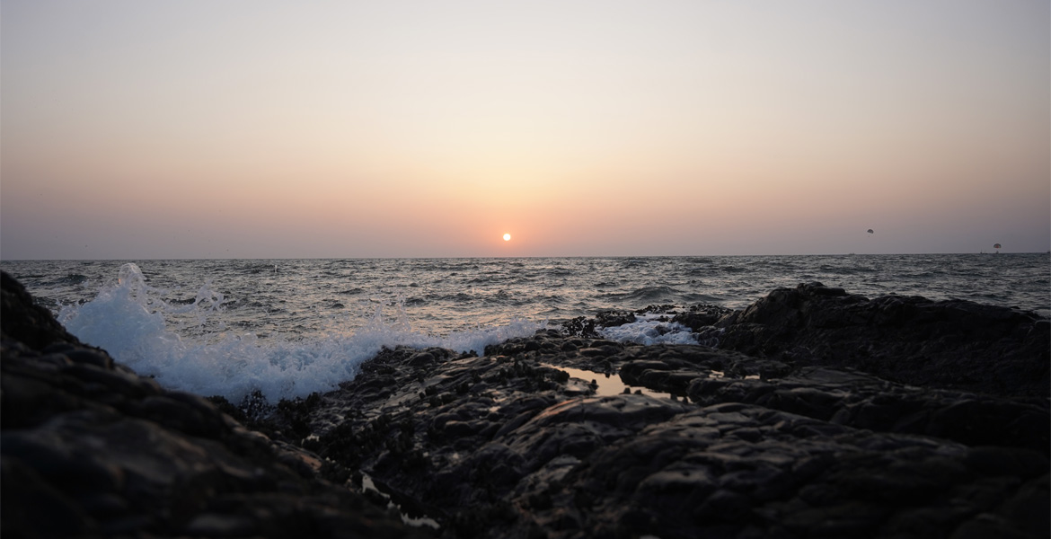 Sunset over the Arabian Sea with waves crashing against the rocky shoreline at Curlies Beach Goa