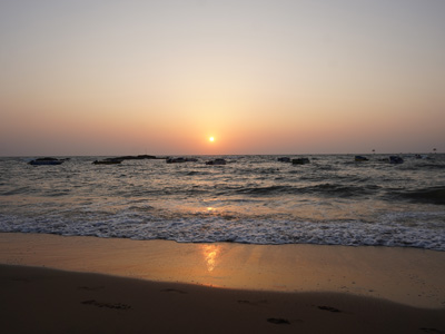 Golden sunset over the Arabian Sea with gentle waves along the sandy shoreline at Curlies Beach Goa