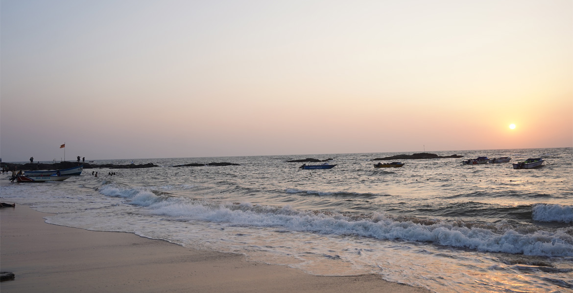 Sunset over the Arabian Sea with fishing boats and gentle waves along the shoreline near Curlies Beach Goa