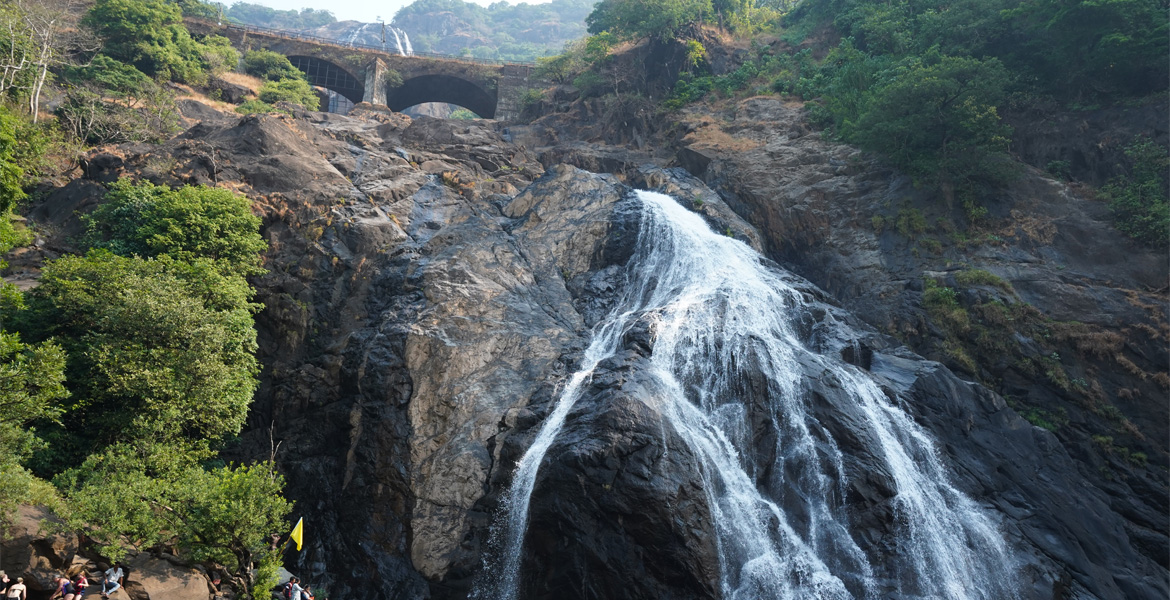 Majestic Dudhsagar Falls cascading over rocky cliffs with the historic railway bridge above in Goa