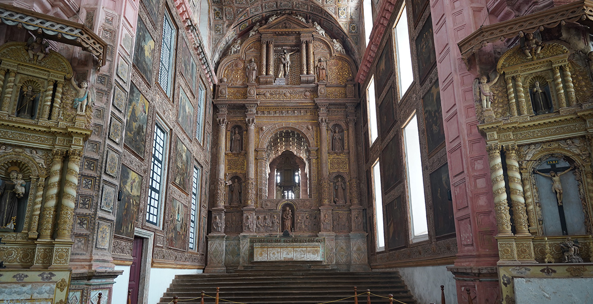 Historic Goa church interior featuring an ornate Baroque altar, carved columns, religious paintings, and detailed architectural design
