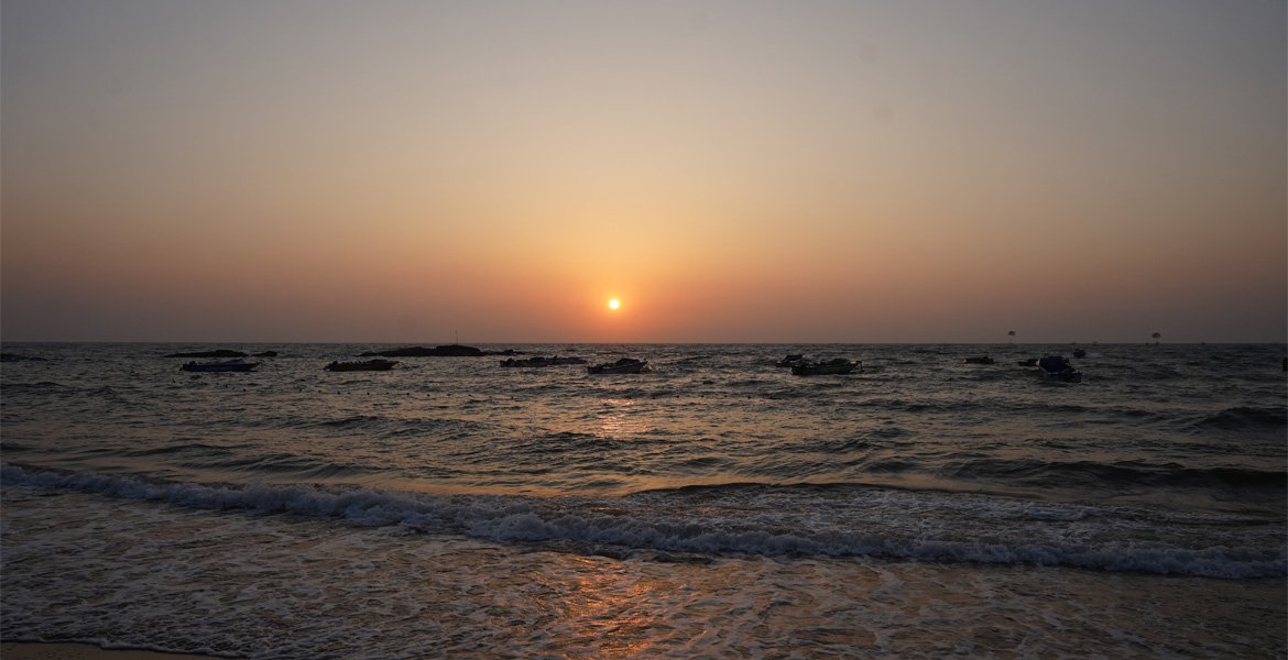 Sunset over a Goa beach with boats on the sea, gentle waves and golden reflections on the water