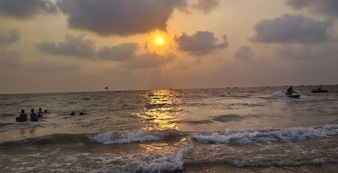 Sunset over a Goa beach with people swimming, waves, water sports and golden reflections on the sea