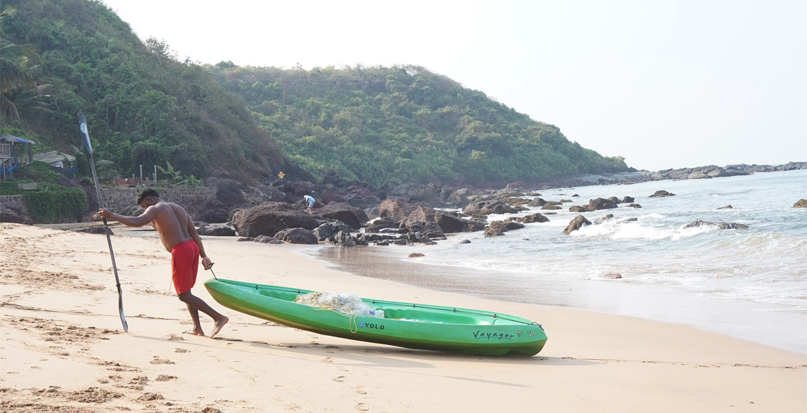 Person carrying a green boat on beach
