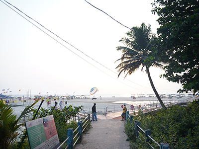 Pathway leading to Majorda Beach Goa with parasailing activity, palm trees, and scenic coastal views