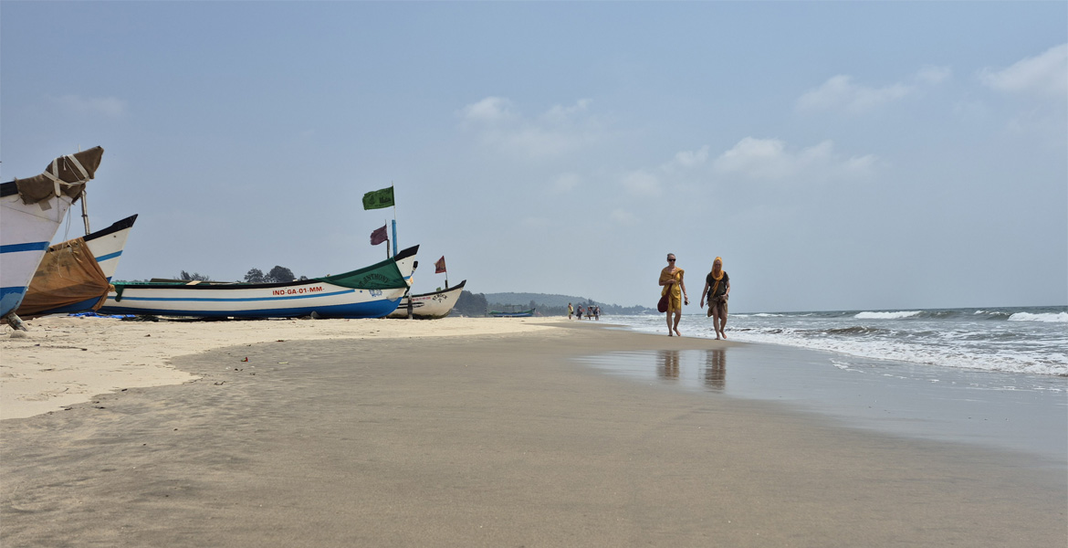 People walking near fishing boats at Mandrem Beach, Goa.