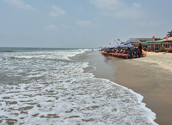 Beautiful shoreline view of Mandrem Beach in Goa with sea waves, beach shacks, and lounge chairs beside the coast