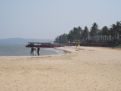 Wide sandy shoreline with palm trees and visitors at Miramar Beach in Goa