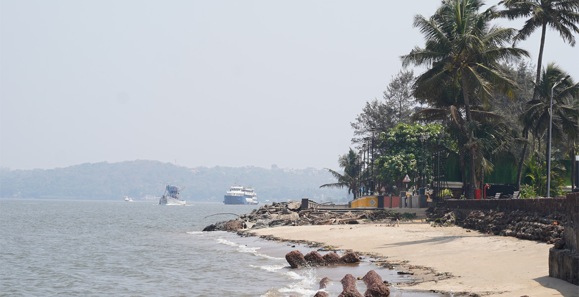 Tourist cruise boats sailing on the water near the palm-lined promenade of Miramar Beach, Goa