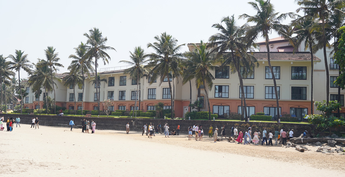 A luxury beachfront resort lined with tall palm trees facing the sandy shore of Miramar Beach, Goa.