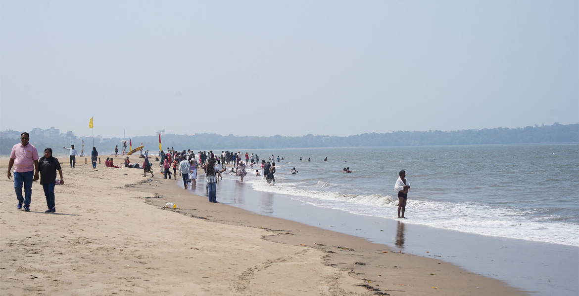Tourists walking and relaxing along the sandy shoreline of Miramar Beach in Goa