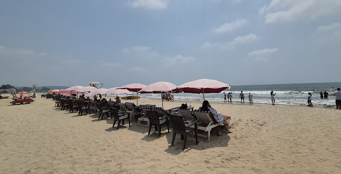 Beachside seating and umbrellas at Morjim Beach in Goa with visitors relaxing near the shoreline and sea waves