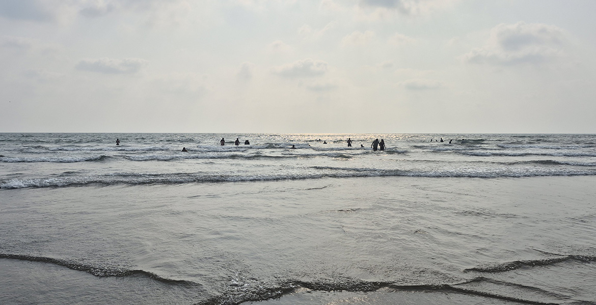 People enjoying the waves at Morjim Beach in Goa during the evening with a calm sea and cloudy sky